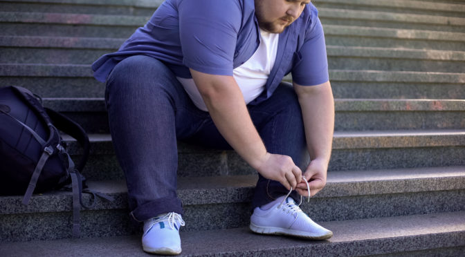 Overweight man sitting on steps to tie shoelaces